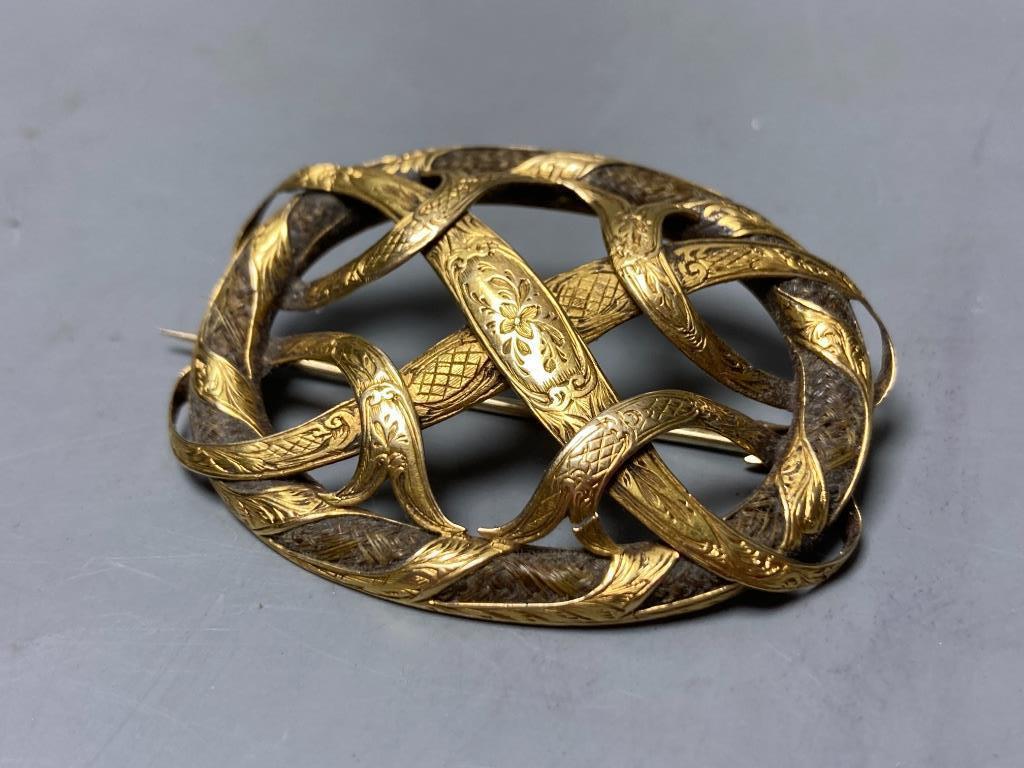 A Victorian engraved yellow metal mounted plaited hair interwoven oval scroll brooch